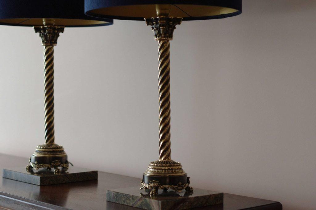 A pair of two luxurious lamps standing on a dresser with beautiful, stylish base in green marble, featuring columns and capitals adorned with stylish acanthus leaf motifs antiqued to an aged bronze finish. Entirely designed and handcrafted at Kostylo atelier